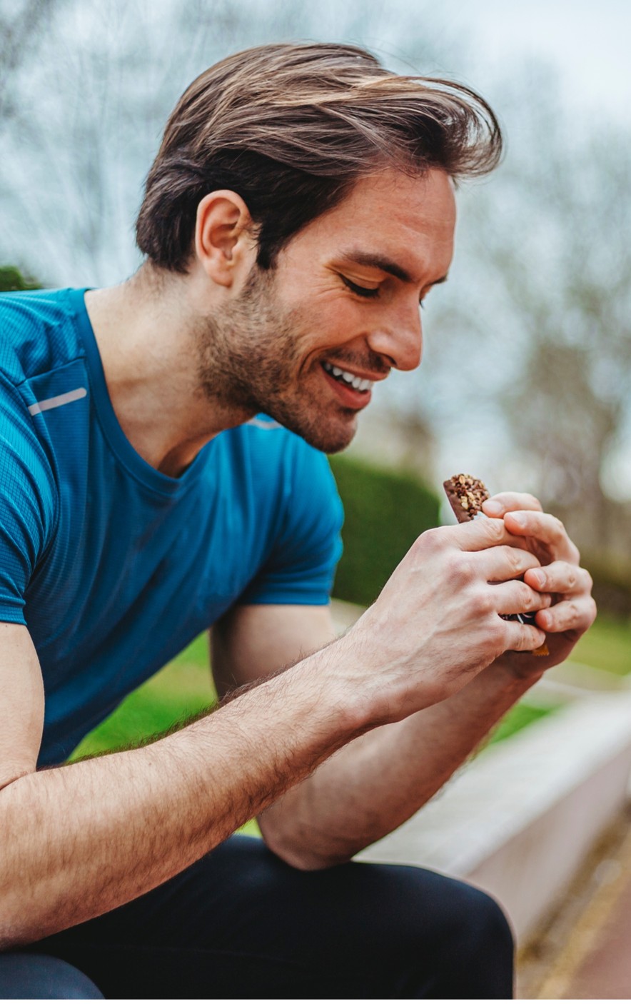 Young man sitting outdoors eating a nutritional bar