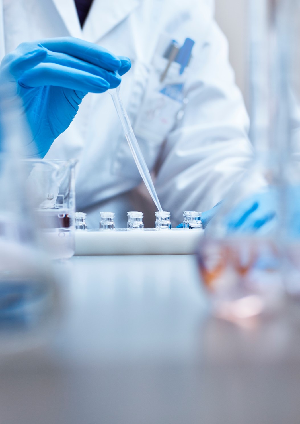Gloved hands of a lab technician operating a pipette