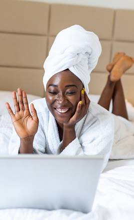 Woman lying on bed after shower, dressed in robe and using laptop