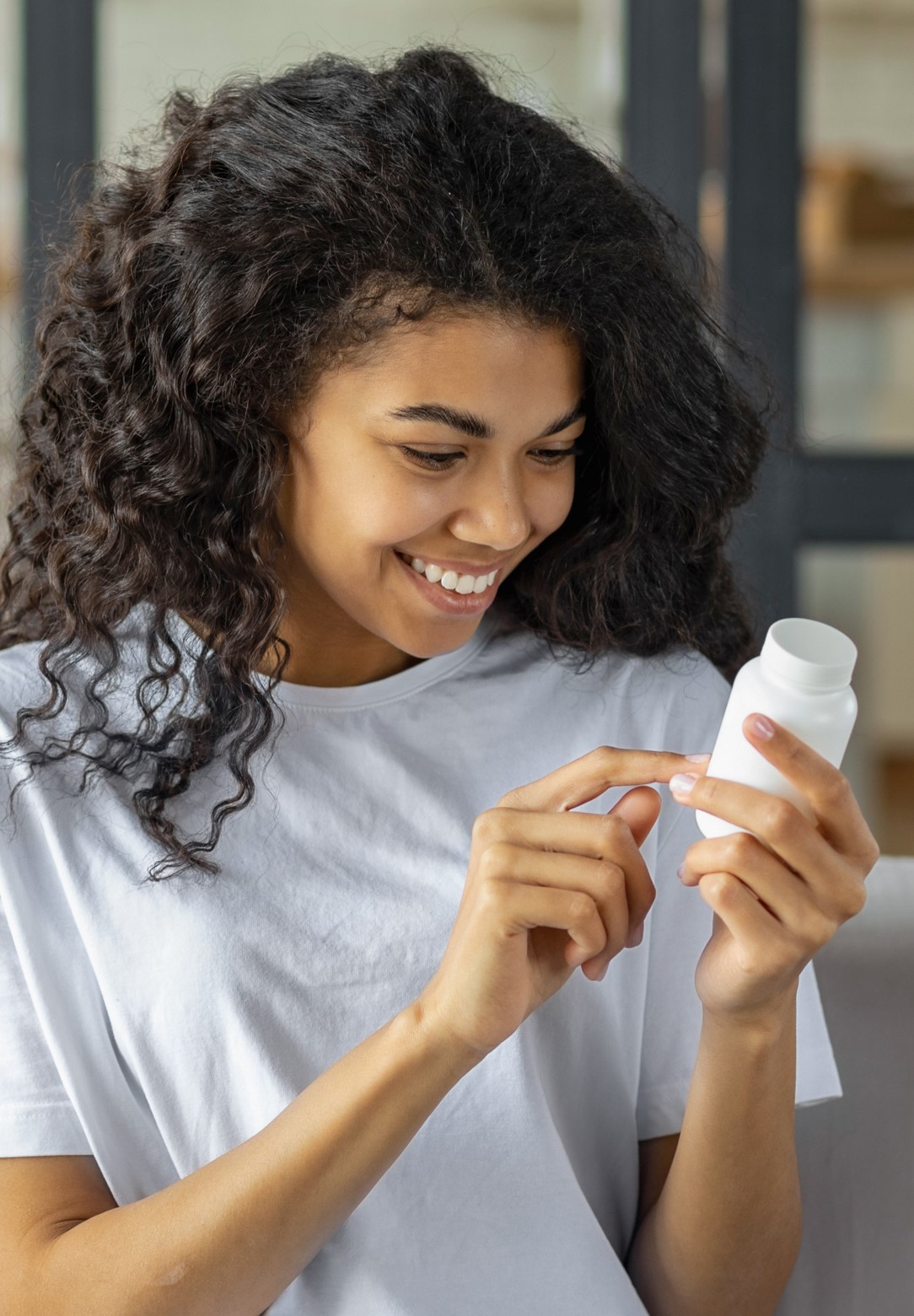 Young Hispanic woman smiling whilst looking at a bottle of capsules