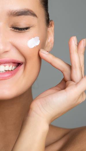 Happy young woman applying moisturising cream to her face