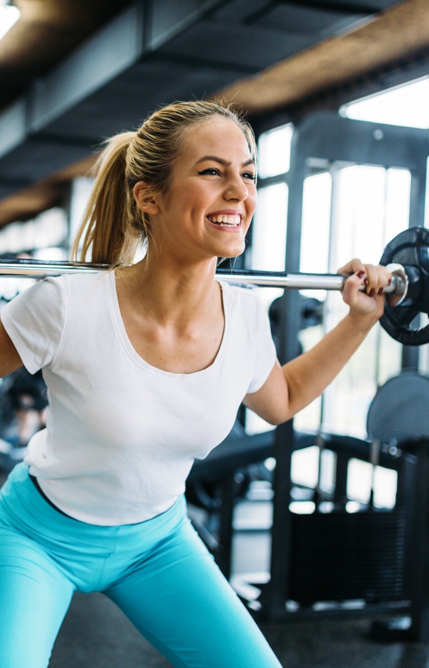 Young Caucasian woman in gym smiling and lifting barbell 