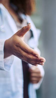 Close up of a woman wearing a white lab coat extending her hand for a handshake.